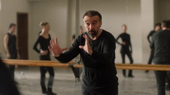 Movie still from “And Then We Danced” (2019), directed by Levan Akin – A man in a black shirt is standing in front of a group of people; Medium shot, Over the shoulder angle