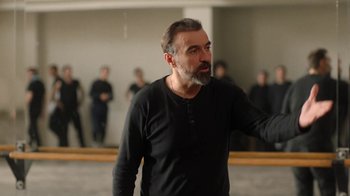 Movie still from “And Then We Danced” (2019), directed by Levan Akin – A man in a black shirt is standing in a room; Medium shot, Over the shoulder angle