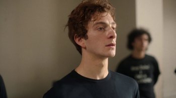 Movie still from “And Then We Danced” (2019), directed by Levan Akin – A young man with brown curly hair wearing a black t - shirt; Close Up shot, Over the shoulder angle