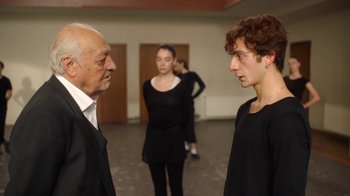 Movie still from “And Then We Danced” (2019), directed by Levan Akin – A man and a woman standing next to each other in front of another man; Medium shot, Over the shoulder angle