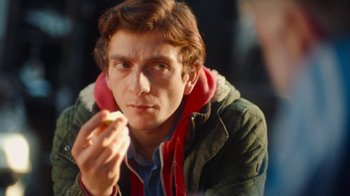 Movie still from “And Then We Danced” (2019), directed by Levan Akin – A man eating a donut while wearing a jacket; Close Up shot, Over the shoulder angle