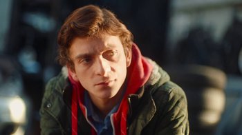 Movie still from “And Then We Danced” (2019), directed by Levan Akin – A young man wearing a green jacket and a red scarf; Close Up shot, Over the shoulder angle