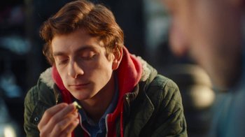 Movie still from “And Then We Danced” (2019), directed by Levan Akin – A young man eating a donut while sitting down; Close Up shot, Over the shoulder angle