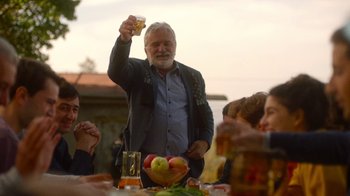Movie still from “And Then We Danced” (2019), directed by Levan Akin – An older man holding up a glass at a table; Medium shot, Low angle