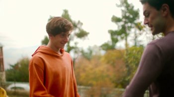 Movie still from “And Then We Danced” (2019), directed by Levan Akin – A young man in an orange hoodie is smiling; Medium shot, Over the shoulder angle
