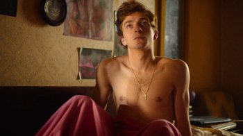 Movie still from “And Then We Danced” (2019), directed by Levan Akin – A young man sitting on a bed with a cross on his chest; Medium shot, High angle
