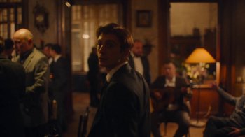 Movie still from “And Then We Danced” (2019), directed by Levan Akin – A man in a suit and tie standing in front of other men; Medium shot, Over the shoulder angle