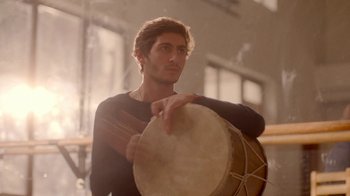 Movie still from “And Then We Danced” (2019), directed by Levan Akin – A man holding a drum while standing in front of a window; Medium shot, Low angle