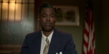 Movie still from “Fargo” (2014), created by Noah Hawley – A man wearing a suit and tie in front of a picture; Close Up shot, High angle