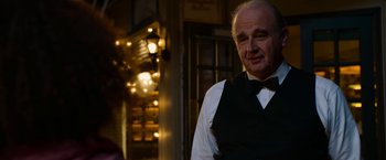 Movie still from “Annie” (2014), directed by Will Gluck – An older man wearing a vest and a bow tie; Close Up shot, Over the shoulder angle