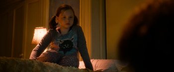 Movie still from “Annie” (2014), directed by Will Gluck – A little girl sitting on a bed in a room; Medium shot, Over the shoulder angle