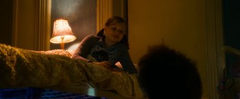 Movie still from “Annie” (2014), directed by Will Gluck – A young girl sitting on a bed in a room; Medium shot, Over the shoulder angle