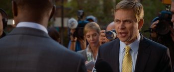 Movie still from “Annie” (2014), directed by Will Gluck – A man in a business suit is being interviewed by reporters; Close Up shot, Over the shoulder angle