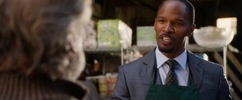 Movie still from “Annie” (2014), directed by Will Gluck – A man in a gray suit and an apron talking; Close Up shot, Over the shoulder angle