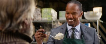 Movie still from “Annie” (2014), directed by Will Gluck – A man in a suit and apron holding a fork and smiling; Close Up shot, Over the shoulder angle