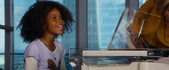 Movie still from “Annie” (2014), directed by Will Gluck – A young girl smiles as she plays the piano; Medium shot, High angle