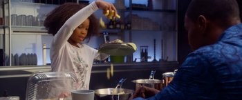 Movie still from “Annie” (2014), directed by Will Gluck – A young girl is putting bananas into a pot; Medium shot, Over the shoulder angle