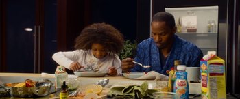 Movie still from “Annie” (2014), directed by Will Gluck – A man and a child eating food at a table; Medium shot, Over the shoulder angle