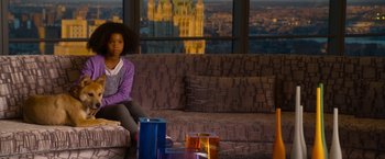 Movie still from “Annie” (2014), directed by Will Gluck – A girl sitting on a couch in front of a large window; Medium shot, Over the shoulder angle