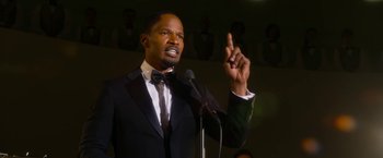 Movie still from “Annie” (2014), directed by Will Gluck – A man wearing a suit and tie holding a microphone; Close Up shot, Low angle