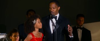 Movie still from “Annie” (2014), directed by Will Gluck – A man and a girl are standing in front of a microphone; Close Up shot, Over the shoulder angle