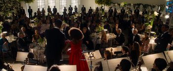 Movie still from “Annie” (2014), directed by Will Gluck – A woman in a red dress standing in front of an orchestra; Extreme Wide shot, Over the shoulder angle