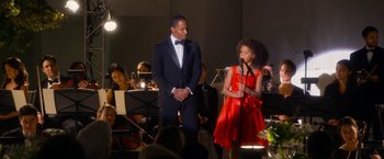 Movie still from “Annie” (2014), directed by Will Gluck – A man and a woman standing next to each other in front of an orchestra; Medium shot, Over the shoulder angle