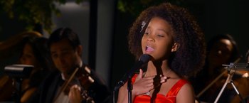 Movie still from “Annie” (2014), directed by Will Gluck – A young girl singing into a microphone while a man plays the violin; Close Up shot, Over the shoulder angle