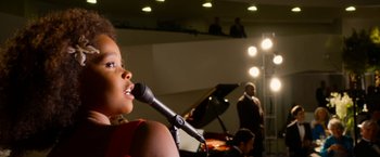 Movie still from “Annie” (2014), directed by Will Gluck – A woman is singing into a microphone in front of an audience; Medium shot, Low angle
