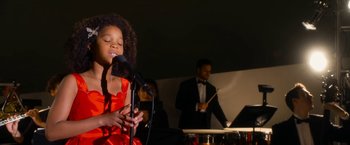 Movie still from “Annie” (2014), directed by Will Gluck – A young girl singing into a microphone while a band plays; Medium shot, Low angle