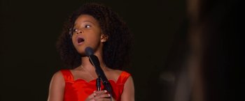Movie still from “Annie” (2014), directed by Will Gluck – A girl in a red dress is holding a microphone; Close Up shot, Low angle