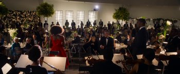 Movie still from “Annie” (2014), directed by Will Gluck – A group of people sitting around a room with musical instruments; Extreme Wide shot, Over the shoulder angle