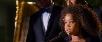 Movie still from “Annie” (2014), directed by Will Gluck – A little girl standing in front of a microphone in front of a man; Close Up shot, Over the shoulder angle