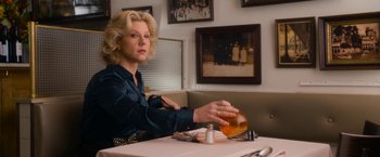 Movie still from “Annie” (2014), directed by Will Gluck – A woman sitting at a table in front of a glass of whiskey; Medium shot, Low angle