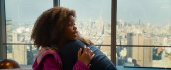 Movie still from “Annie” (2014), directed by Will Gluck – A young girl holding a stuffed animal in front of a large window; Close Up shot, Over the shoulder angle