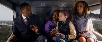 Movie still from “Annie” (2014), directed by Will Gluck – Two young girls and an older man are sitting on a plane; Medium shot, High angle