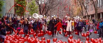 Movie still from “Annie” (2014), directed by Will Gluck – A group of people marching down a street with red balloons; Extreme Wide shot, High angle