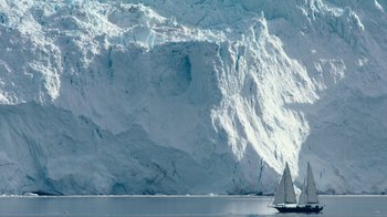 A sailboat in front of a large glacier in the ocean