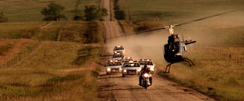 Movie still from “Armageddon” (1998), directed by Michael Bay – A group of police cars driving down a dirt road next to a helicopter; Extreme Wide shot, High angle