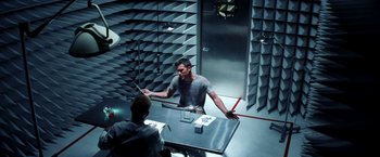 Movie still from “Armageddon” (1998), directed by Michael Bay – Two men are sitting at a table in a room; Wide shot, High angle