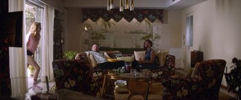 Movie still from “Assassination Nation” (2018), directed by Sam Levinson – A man and a woman sitting on couches in a living room; Wide shot, High angle