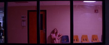 Movie still from “Assassination Nation” (2018), directed by Sam Levinson – A woman sitting on a chair in a room with pink lighting; Wide shot, Low angle