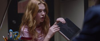 Movie still from “Assassination Nation” (2018), directed by Sam Levinson – A woman with red hair is holding a book; Medium shot, Over the shoulder angle