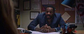 Movie still from “Assassination Nation” (2018), directed by Sam Levinson – A man sitting at a desk in front of papers; Medium shot, Over the shoulder angle