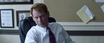 Movie still from “Assassination Nation” (2018), directed by Sam Levinson – A man sitting in a chair wearing a white shirt and a red tie; Close Up shot, Over the shoulder angle