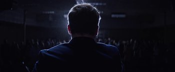 Movie still from “Assassination Nation” (2018), directed by Sam Levinson – A man in a black jacket is in a dark room; Medium shot, Low angle