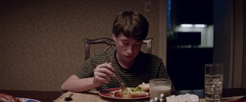 Movie still from “Assassination Nation” (2018), directed by Sam Levinson – A young man sitting at a table eating food; Close Up shot, Over the shoulder angle