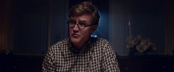 Movie still from “Assassination Nation” (2018), directed by Sam Levinson – A man wearing glasses sitting in a room; Close Up shot, Over the shoulder angle