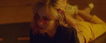 Movie still from “Assassination Nation” (2018), directed by Sam Levinson – A woman with blonde hair wearing sunglasses and a pink flower in her hair; Close Up shot, Over the shoulder angle