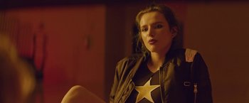 Movie still from “Assassination Nation” (2018), directed by Sam Levinson – A woman sitting on the ground with a star on her shirt; Close Up shot, Over the shoulder angle
